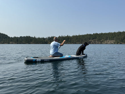 Paddler kneeling on a Hydrus JoyRide XL with his black lab on a calm lake