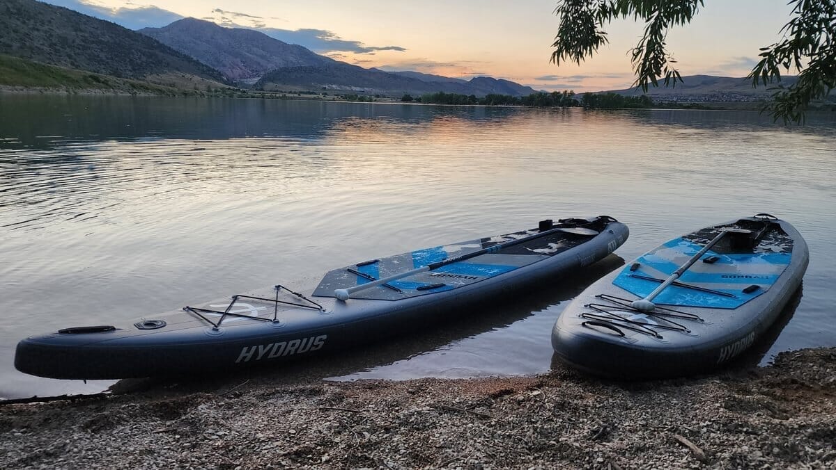 A paddleboard spec sheet with the five decision-driving specs highlighted (width, length, thickness, construction, fin setup) and the marketing-fluff specs faded, illustrating which numbers actually predict how a board paddles.