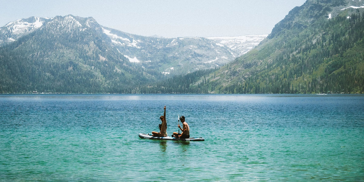 Two paddlers on a Hydrus inflatable paddle board on a turquoise mountain lake