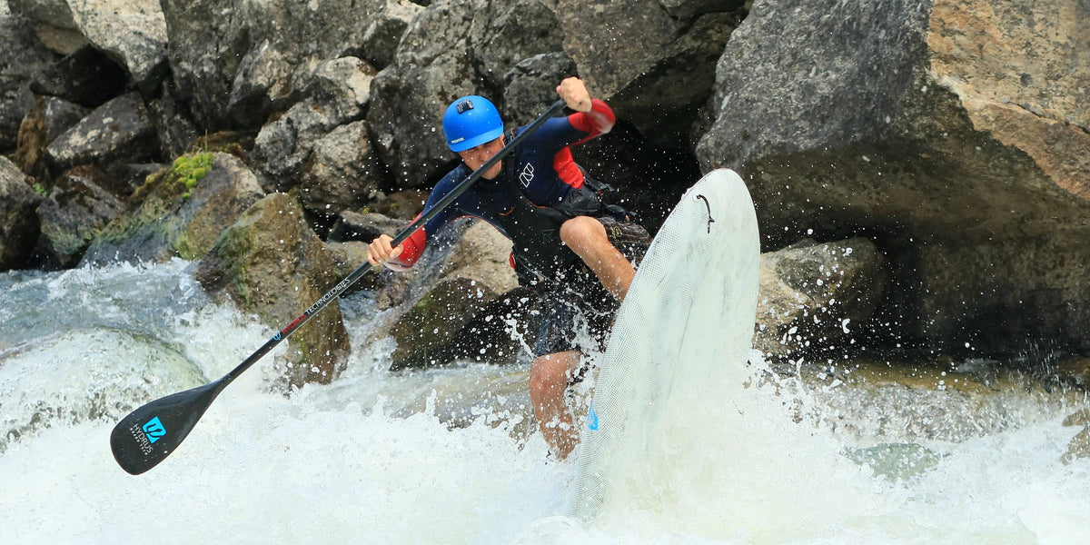 Paddler in a helmet punching through whitewater on a surf paddle board